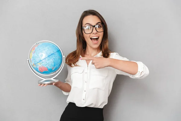 Portrait of an excited young business woman pointing finger at earth globe isolated over white background
