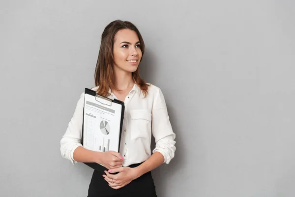 灰色の壁背景持株クリップボードに分離立って驚くほど陽気な若いビジネス女性のイメージ — ストック写真