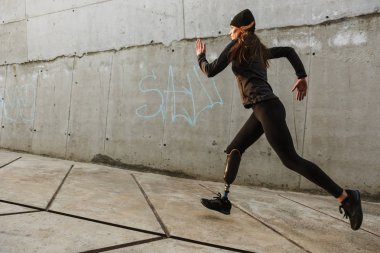 Beton duvar boyunca açık çalıştıran eşofman Protez bacak ile Engelli sporcu kadın portresi