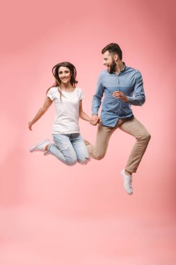 Ellerini tutarken atlama üzerinde pembe arka plan izole mutlu bir genç çift tam uzunlukta portresi