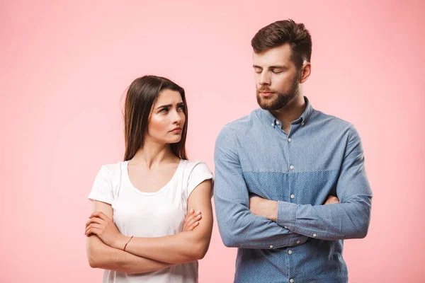 Portrait of an angry young couple standing with arms folded isolated over pink background