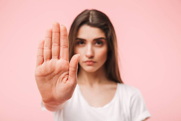 Portrait of a confident young woman showing stop gesture with her palm isolated over pink background