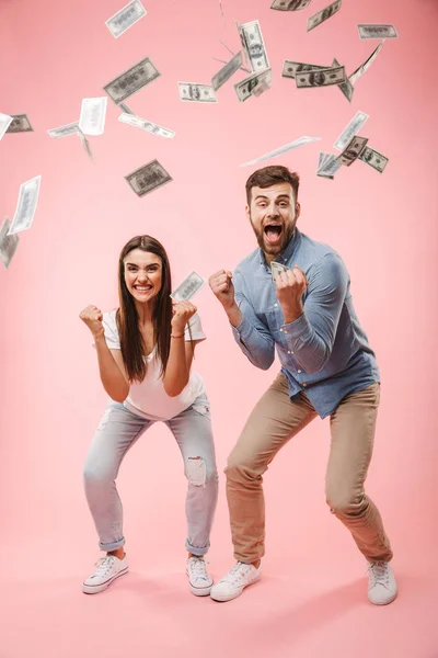 一个兴奋的年轻夫妇站在钞票的全长肖像淋浴和庆祝成功隔离粉红色背景 — 图库照片