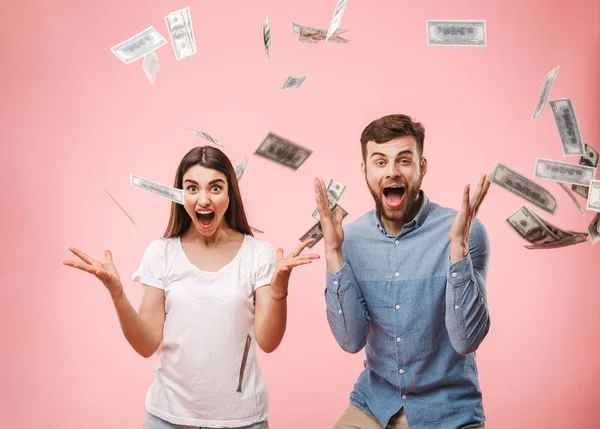 一个快乐的年轻夫妇站在钞票上的肖像淋浴和庆祝成功隔离粉红色背景 — 图库照片
