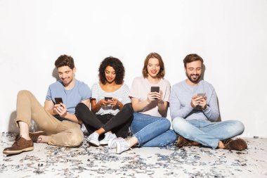 Gruba konfeti ile bir katta oturan ve cep telefonları üzerinde beyaz arka plan izole kullanarak mutlu çok ırklı