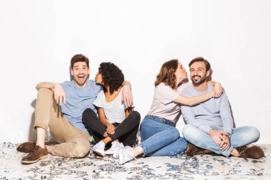Konfeti ve beyaz arka plan üzerinde izole sarılma bir katta oturan mutlu çok ırklı kişilik grup