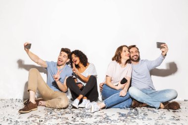 Gruba konfeti ile bir katta oturan ve beyaz arka plan üzerinde izole selfies alarak mutlu çok ırklı