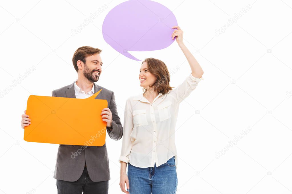 Portrait of a smiling young business couple holding empty speech bubbles isolated over white background