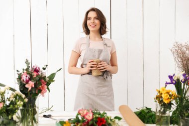 Tablo farklı çiçek ve bir kenara atölyede seyir ile yakın duran çiçekçi kadın gülümseyen bir görüntü.