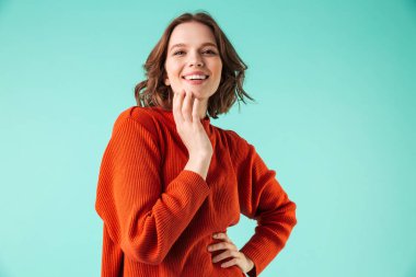 Gülünecek bir genç kadının portresi üzerinde mavi arka plan izole kamera bakarak kazak giymiş