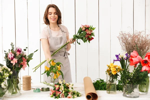 別の花のワーク ショップでよそ見とテーブルの近くに立っている花屋の女性の笑顔のイメージ — ストック写真