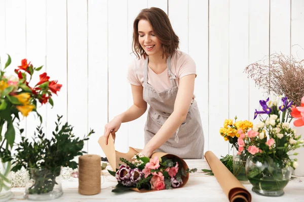 ワーク ショップの花で作業中のテーブルの近くに立って幸せな花屋の女性の写真 — ストック写真