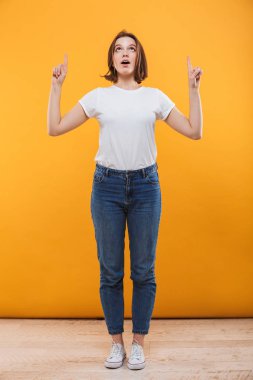 Heyecanlı genç kadın bir kenara boşaltmak seyir gösterilen sarı arka plan üzerinde izole ayakta görüntüsünü.