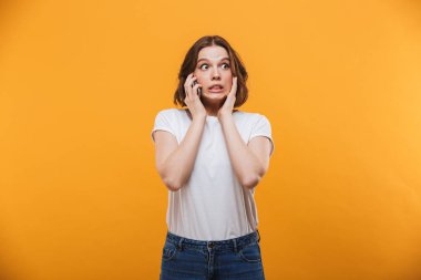 Cep telefonuyla konuşurken sarı arka plan üzerinde izole ayakta sinir genç kadın görüntüsü. Bir kenara arıyorsunuz