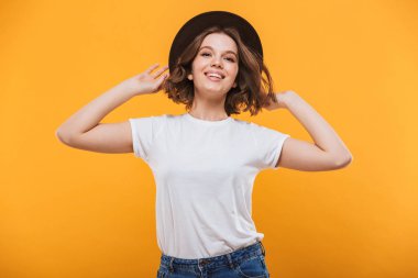 Görüntü izole kamera seyir sarı arka plan üzerinde duran neşeli giyen genç kadın şapka.