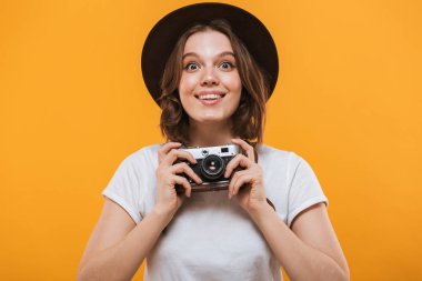 Görüntü izole kamera tutarak sarı arka plan üzerinde duran heyecanlı duygusal genç kadın fotoğrafçı turist.