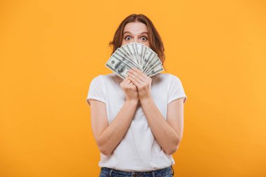 Yüz kapsayan para tutan sarı arka plan üzerinde izole duran duygusal genç kadın görüntüsünü.
