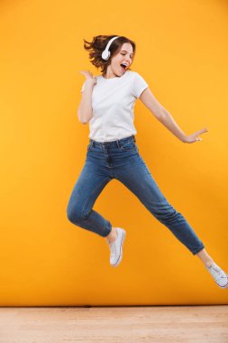 Duygusal komik genç kadının atlama görüntü izole sarı arka plan müzik dinleme.