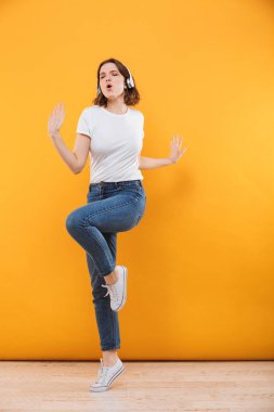 Tam uzunlukta kulaklık ile müzik dinlemek ve sarı arka plan üzerinde dans kazaklı memnun genç bir kadın portresi