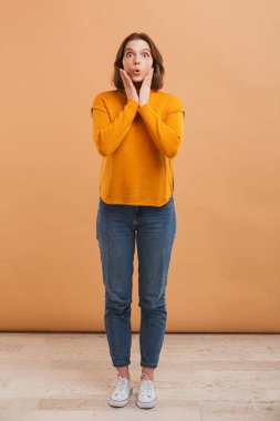 Tam uzunlukta sarı arka plan üzerinde kameraya bakarak kazaklı heyecanlı bir genç kadın portresi