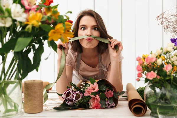 ワーク ショップの花で作業中のテーブルの近くに立ってかわいい面白い花屋女性の写真 カメラを探しています — ストック写真