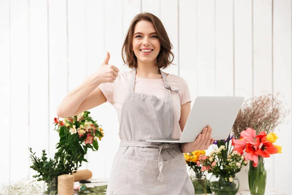 お花屋さんで花束の近くに立って 手にノート パソコン親指を示す販売の女性を笑顔 — ストック写真