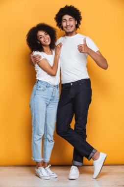 Ayakta ve sarı arka plan üzerinde izole jest Yaşasın gösterilen bir gülümseyen genç afro Amerikan çift tam uzunlukta portresi