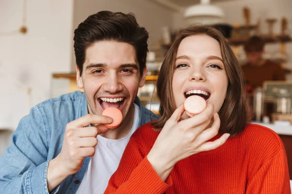 Portrait of beautiful happy couple man and woman looking at camera and eating macaron biscuits