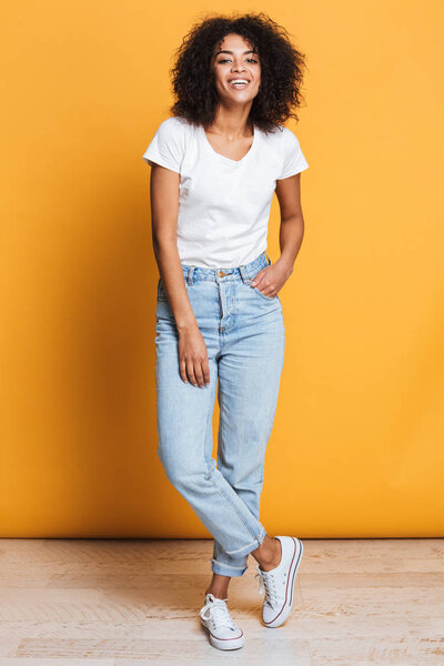 Полный портрет улыбающейся молодой африканской женщины, смотрящей на камеру, изолированную на жёлтом фоне
