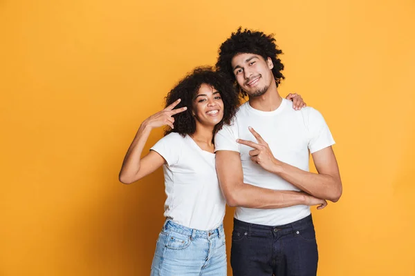 Portrait of a happy afro american couple showing peace gesture isolated over yellow background