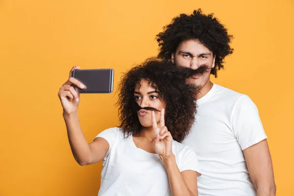 Portrait of a funny young afro american couple taking a selfie isolated over yellow background