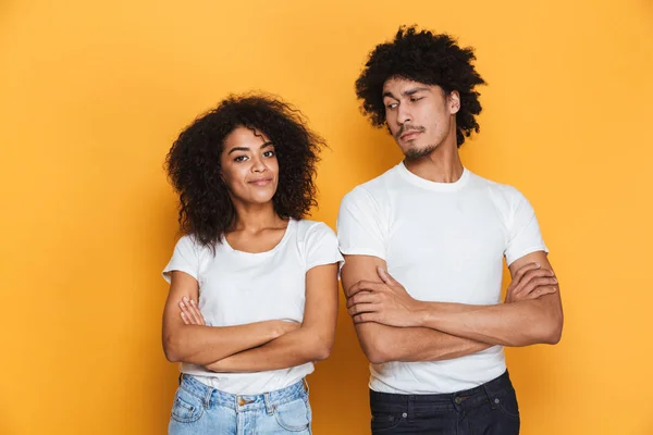 Portrait of a smiling young afro american couple standing with arms folded isolated over yellow background