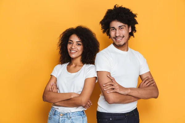 Portrait of a happy young afro american couple standing with arms folded isolated over yellow background