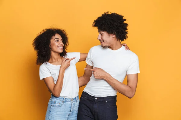 Portrait of a lovely young afro american couple pointing fingers at each other isolated over yellow background