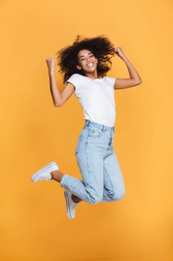 Neşeli bir genç Afrikalı kadın atlama izole sarı arka plan üzerinde iken başarı kutluyor tam uzunlukta portresi