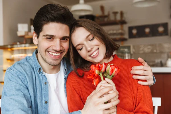 一张照片 一对年轻的情侣男女举行美丽的花朵一起坐在餐桌上 在舒适的咖啡馆 — 图库照片