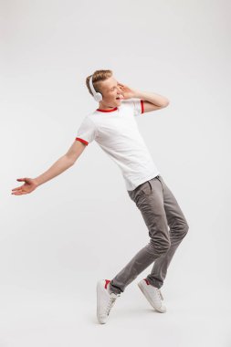Neşeli çocuk casual giyim dans ve beyaz arka plan üzerinde izole kulaklık aracılığıyla müzik dinlerken şarkı tam uzunlukta portresi