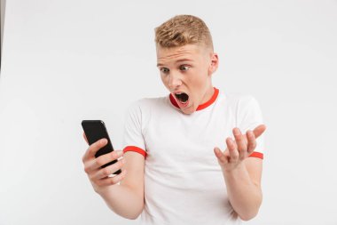 Rahat tarzı süre tutarak ve beyaz arka plan üzerinde izole smartphone kullanarak çığlık giyen öfkeli genç adam fotoğrafı