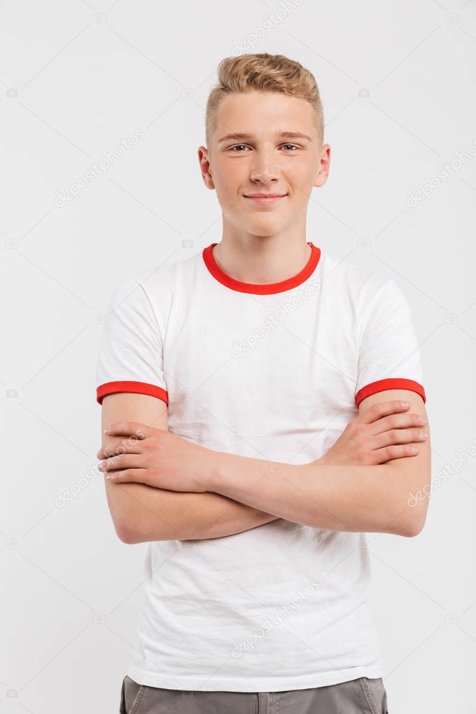 Portrait of a smiling teenage boy standing with arms folded isolated over white background