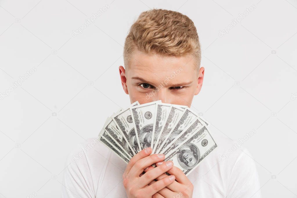 Portrait of a happy teenage boy holding money banknotes at his face isolated over white background