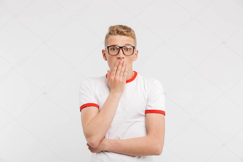 Photo of scared guy in eyeglasses looking at you and covering mouth in fear or shock isolated over white background