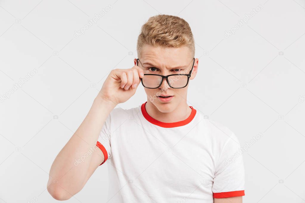 Portrait of a suspicious teenage boy in eyeglasses looking at camera isolated over white background