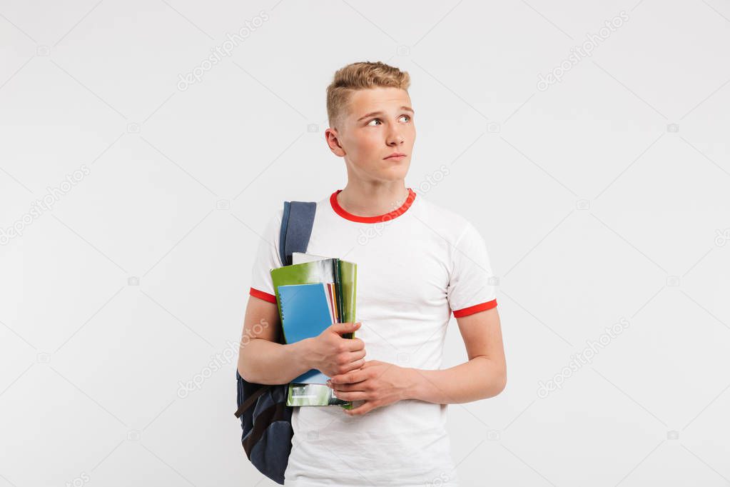 Image of young guy university or college student wearing backpack looking aside at copyspace while holding textbooks isolated over white background
