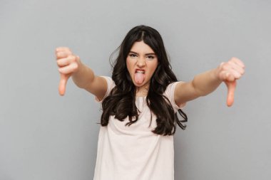 Memnun genç bayan ayakta başparmak aşağı gösterilen gri arka plan duvar üzerinde izole görüntüsünü.