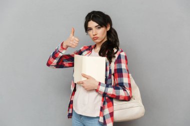 Görüntü izole kitap jest yapmak Yaşasın tutan gri arka plan duvar üzerinde duran güzel sevimli genç bayan öğrenci.