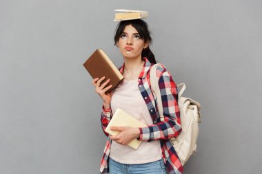 Kitap gri arka plan duvardan izole duran genç bayan öğrenci üzücü görüntüsünü sıktı.