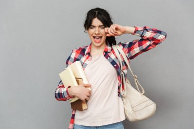 Görüntü izole kitap cry tutan gri arka plan duvardan ayakta üzgün memnun genç bayan öğrenci.