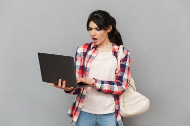 Dizüstü bilgisayar kullanan gri arka plan duvardan izole üzgün memnun genç bayan öğrenci görüntüsünü.