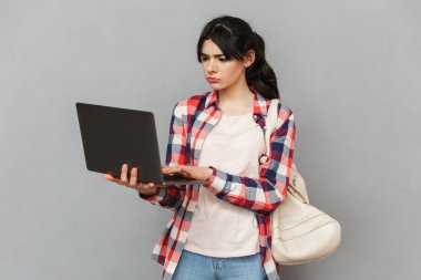 Dizüstü bilgisayar kullanan gri arka plan duvardan izole üzgün memnun genç bayan öğrenci görüntüsünü.