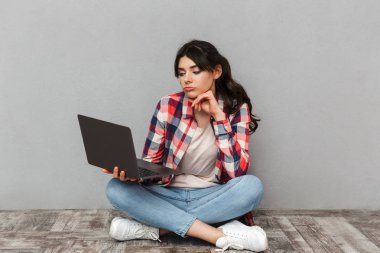 Dizüstü bilgisayar kullanan gri arka plan duvardan izole üzgün memnun genç bayan öğrenci görüntüsünü.